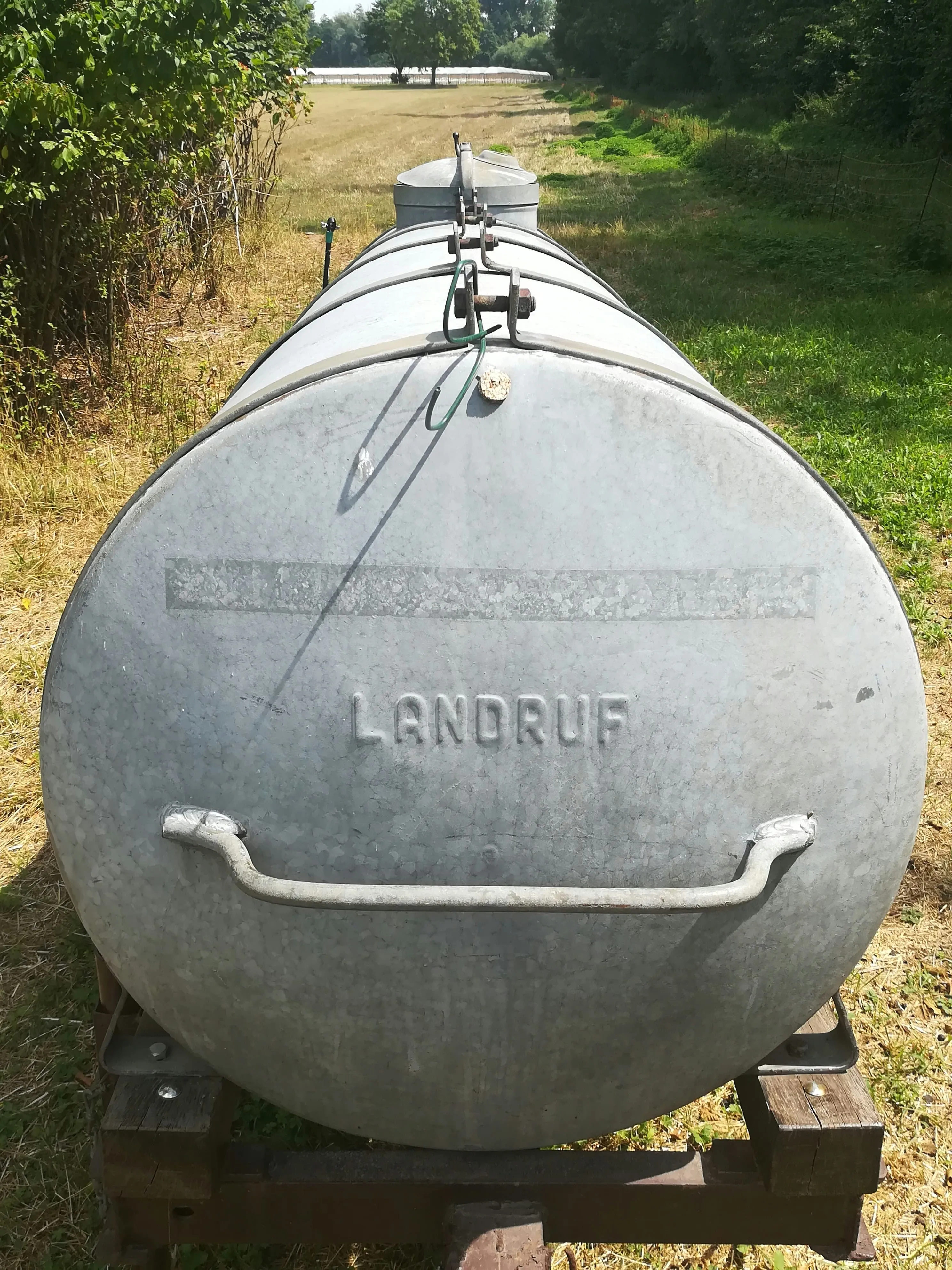 A large galvanized steel water tank in a field — the kind of holding tank serviced when removing and disposing of gray water from food trucks and RVs