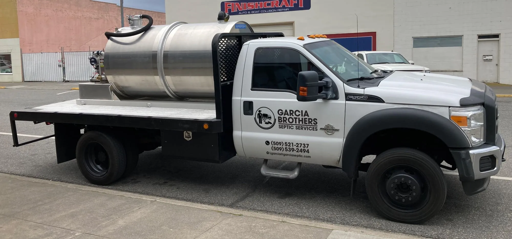 The Garcia Brothers Portable Toilet Rentals white flatbed truck fitted with a polished stainless-steel vacuum tank, branded with the company logo and phone number